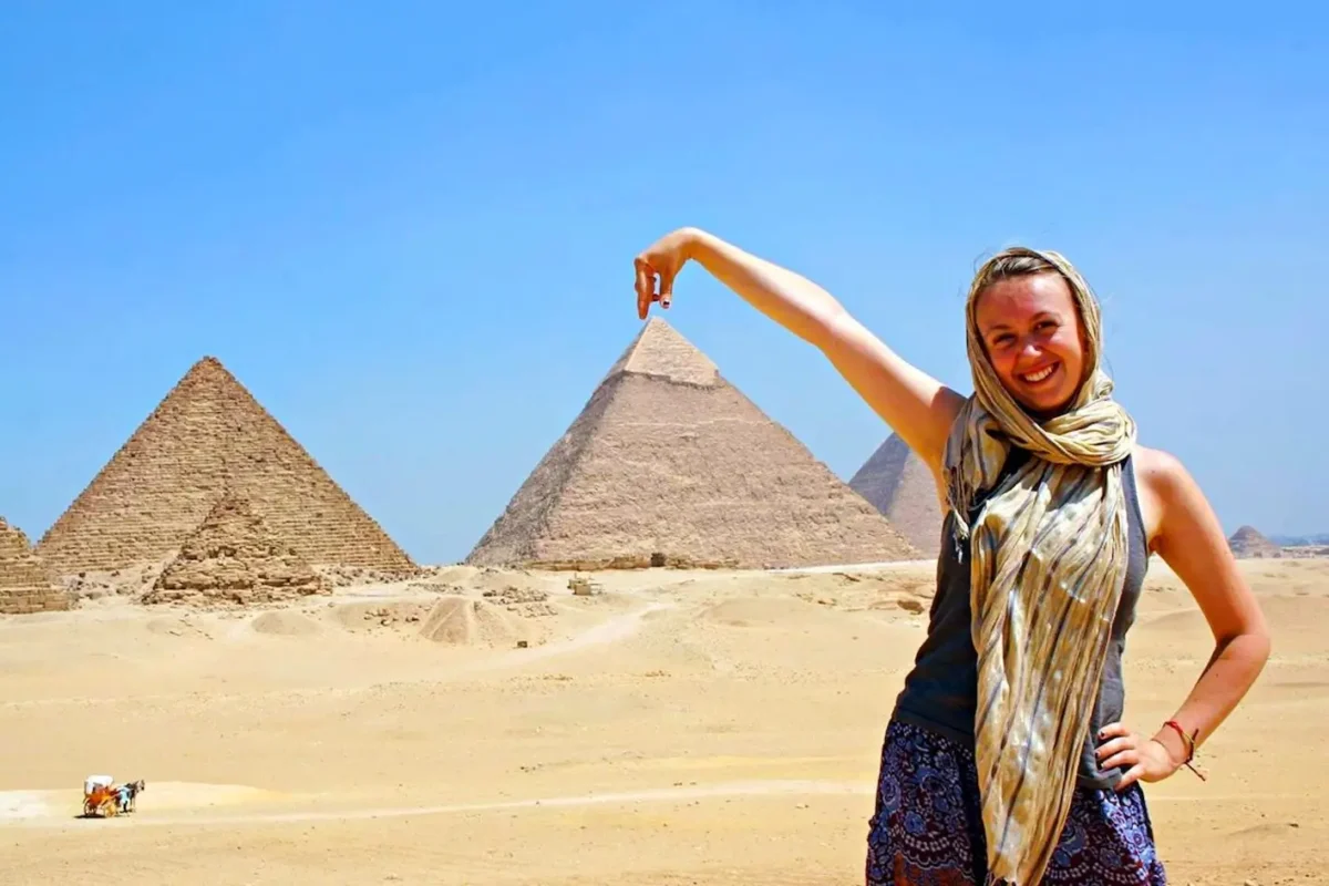 A woman posing for a forced-perspective photograph with the three pyramids of Giza behind her