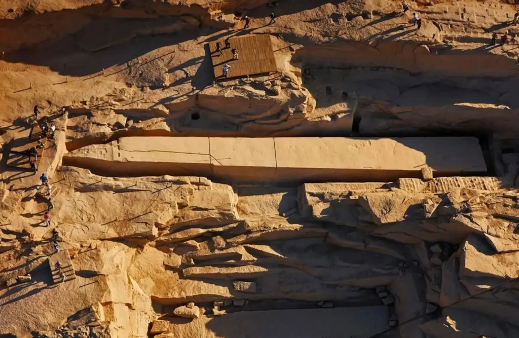 The full length of the Unfinished Obelisk seen from the rim of the Aswan granite quarry, visitors along the path beside it