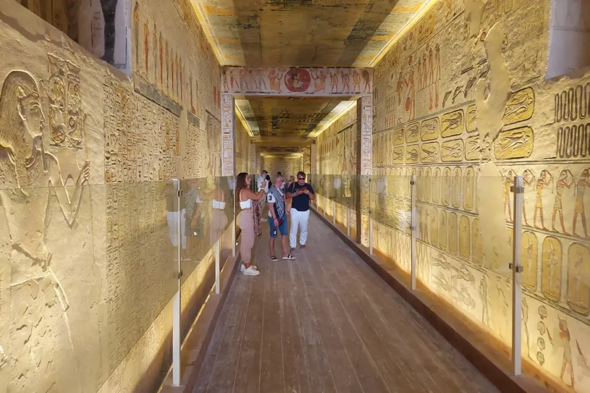 Visitors walking a tomb corridor in the Valley of the Kings, carved and painted reliefs covering both walls
