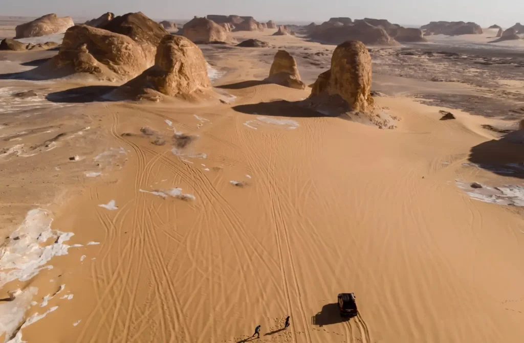 The chalk formations of the White Desert seen from above, a vehicle and its tracks crossing the sand between them