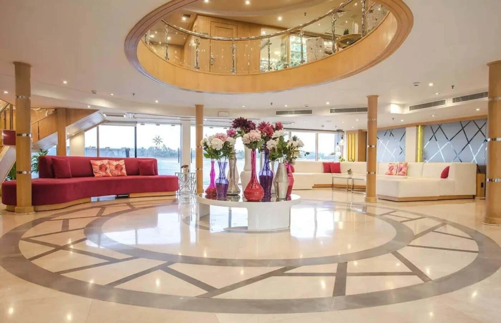 The atrium lobby of the MS Acamar Nile cruise, an inlaid marble floor beneath a circular balcony opening, red sofas and tall flower vases
