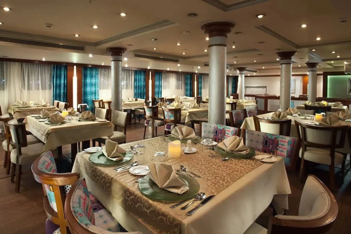 The restaurant on the MS Acamar Nile cruise, tables laid with candles and folded napkins between panelled columns