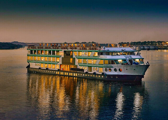 The MS Acamar Nile cruise ship lit from within at dusk, its reflection running across still water