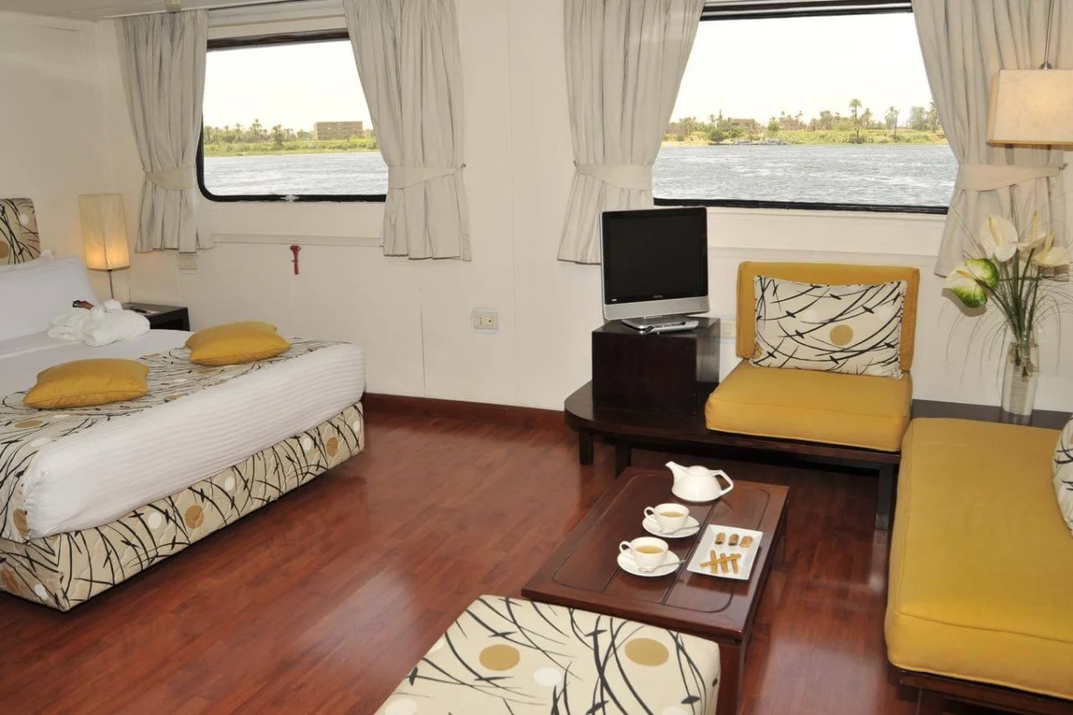 A suite on the MS Alexander the Great Nile cruise with a seating area in yellow, a low table set with tea and two windows onto the Nile