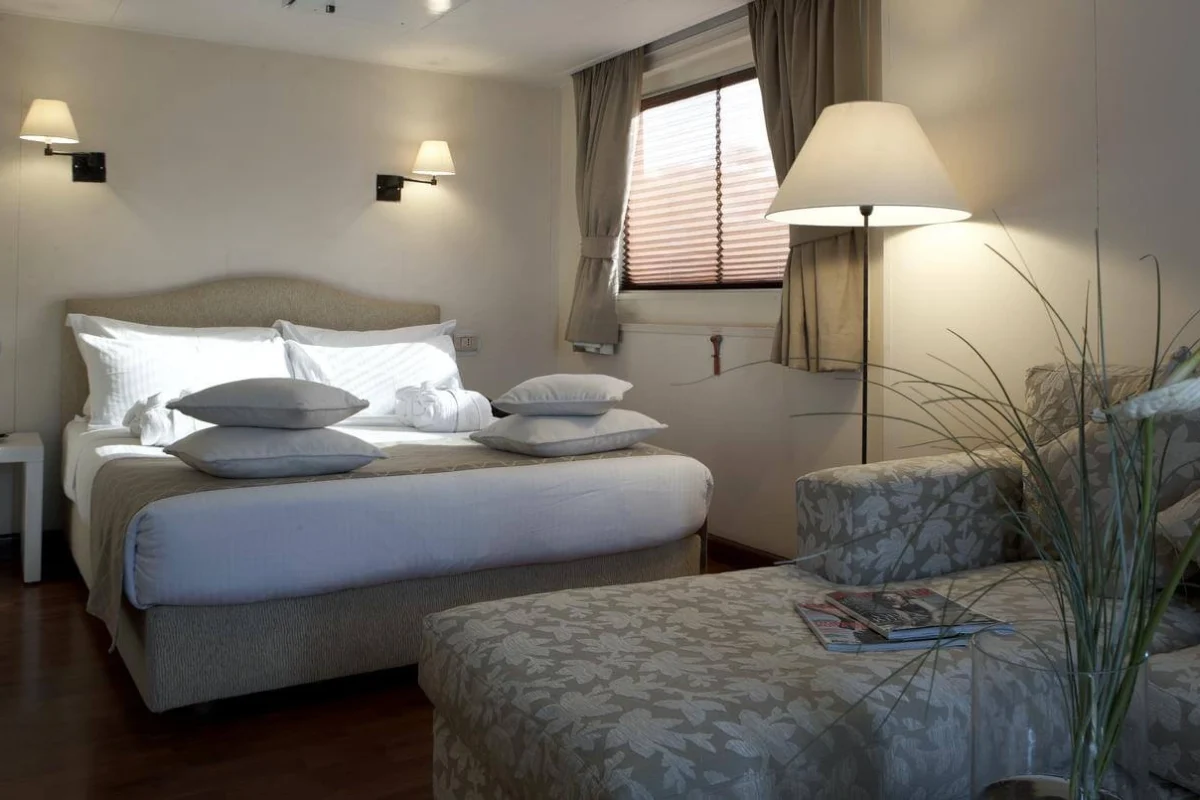 A twin-bed cabin on the MS Alexander the Great Nile cruise with grey linen, reading lights above the beds and an armchair by the window