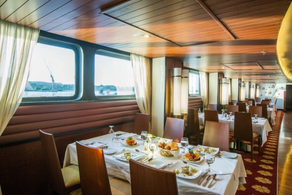 Tables laid with salads and glassware in the Alyssa Nile cruise restaurant, banquette seating beneath windows onto the Nile