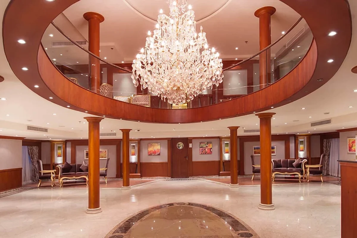 A crystal chandelier hanging through the circular atrium opening of the MS Amwaj Living Stone Nile cruise, timber columns around a marble floor