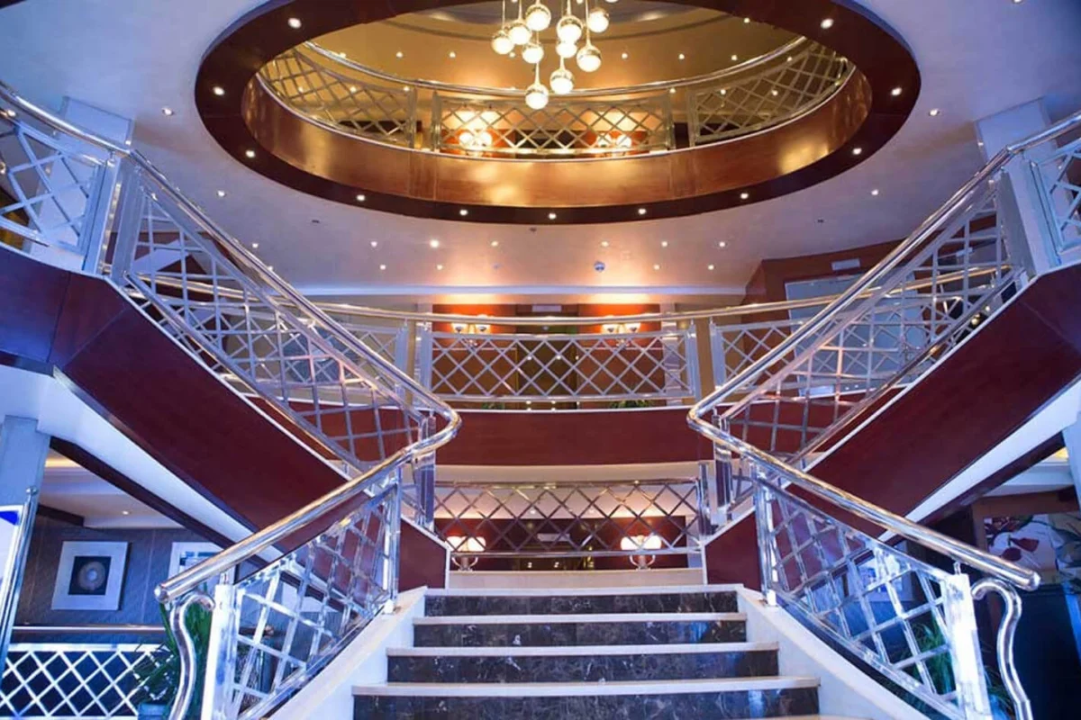 The twin staircase of the Blue Shadow Nile cruise atrium rising beneath a domed ceiling and chandelier