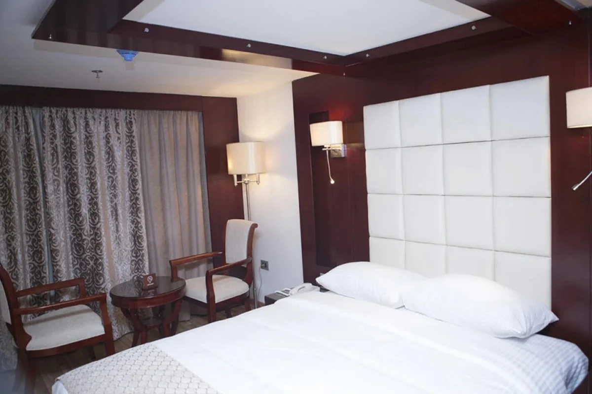 A double cabin on the Blue Shadow Nile cruise with a padded white headboard, reading lamps and two chairs at the curtained window