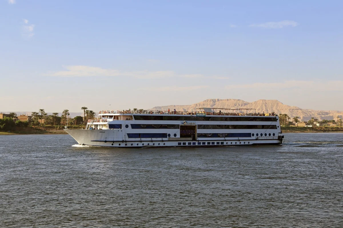 The Blue Shadow Nile cruise ship under way on the Nile, palms on the near bank and desert hills behind