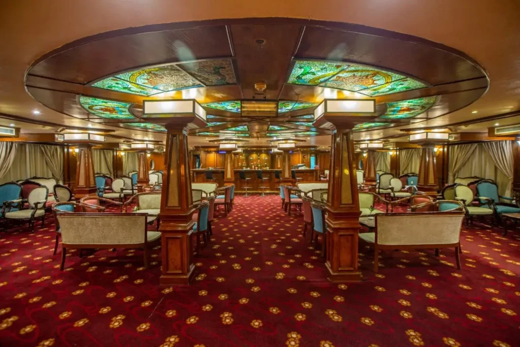 The lounge on the Chateau Lafayette Nile cruise, armchairs on a red patterned carpet beneath a stained-glass ceiling