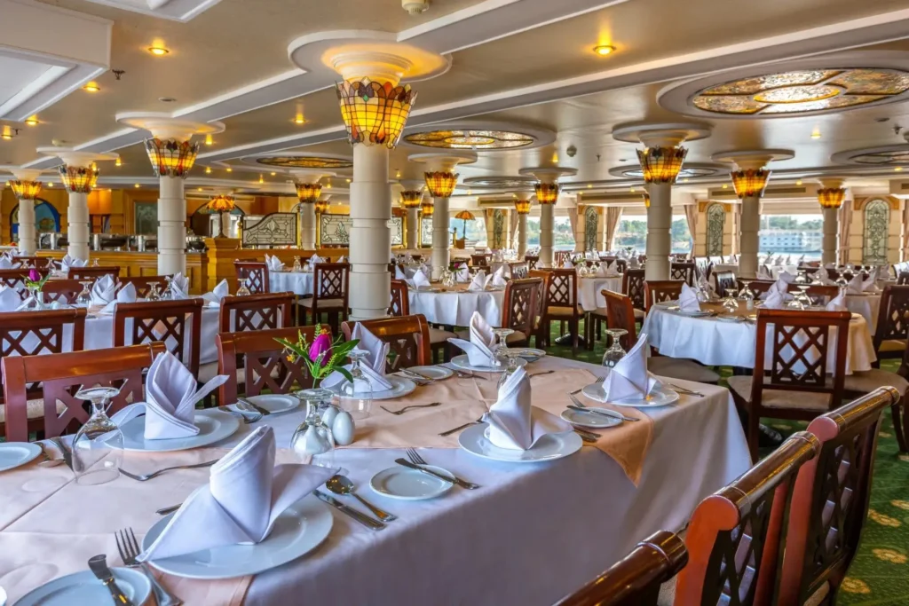 The restaurant on the Chateau Lafayette Nile cruise, white-clothed tables between carved columns under a stained-glass ceiling
