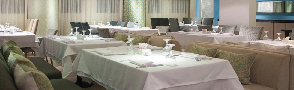 Tables laid with white linen in the Farida Nile cruise restaurant, upholstered chairs and daylight from the river windows