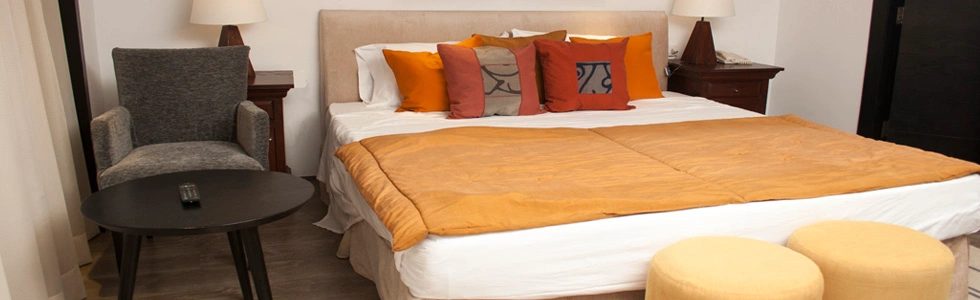 A suite bedroom on the Farida Nile cruise, a wide bed dressed in orange with cushions, an armchair and two ottomans