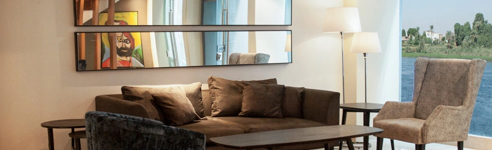 The sitting area of a suite on the Farida Nile cruise, a corner sofa and armchair beside a window onto the Nile