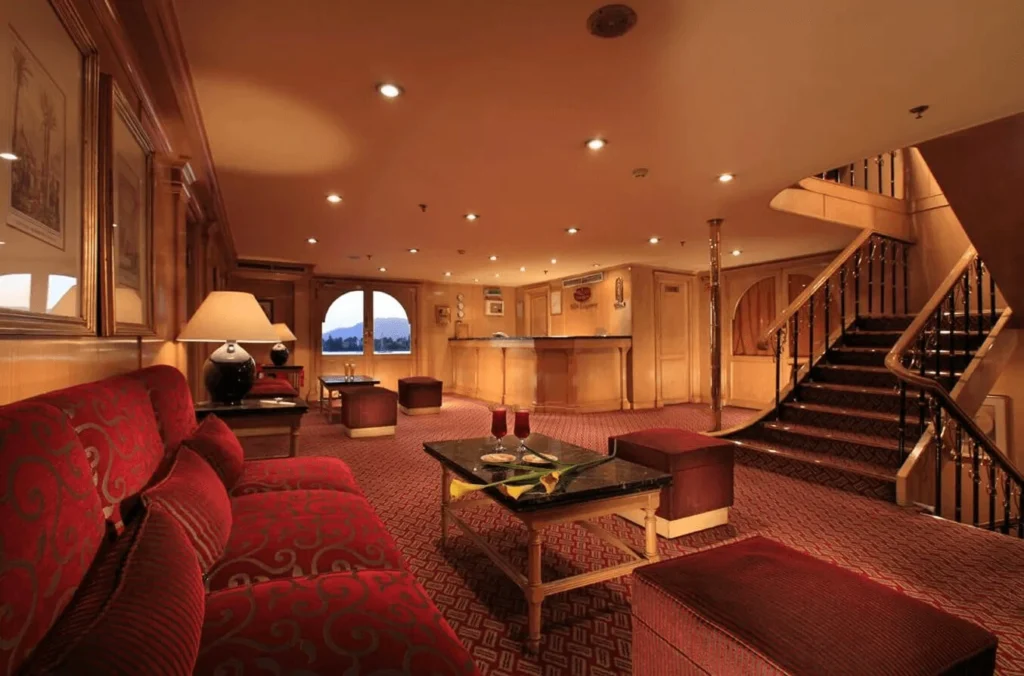 The lobby of the Iberotel Amara Nile cruise, a red sofa and coffee table beside the timber staircase to the upper deck