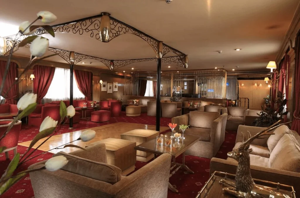 The main lounge of the Iberotel Amara Nile cruise, sofas and armchairs on a red carpet beneath an ironwork canopy