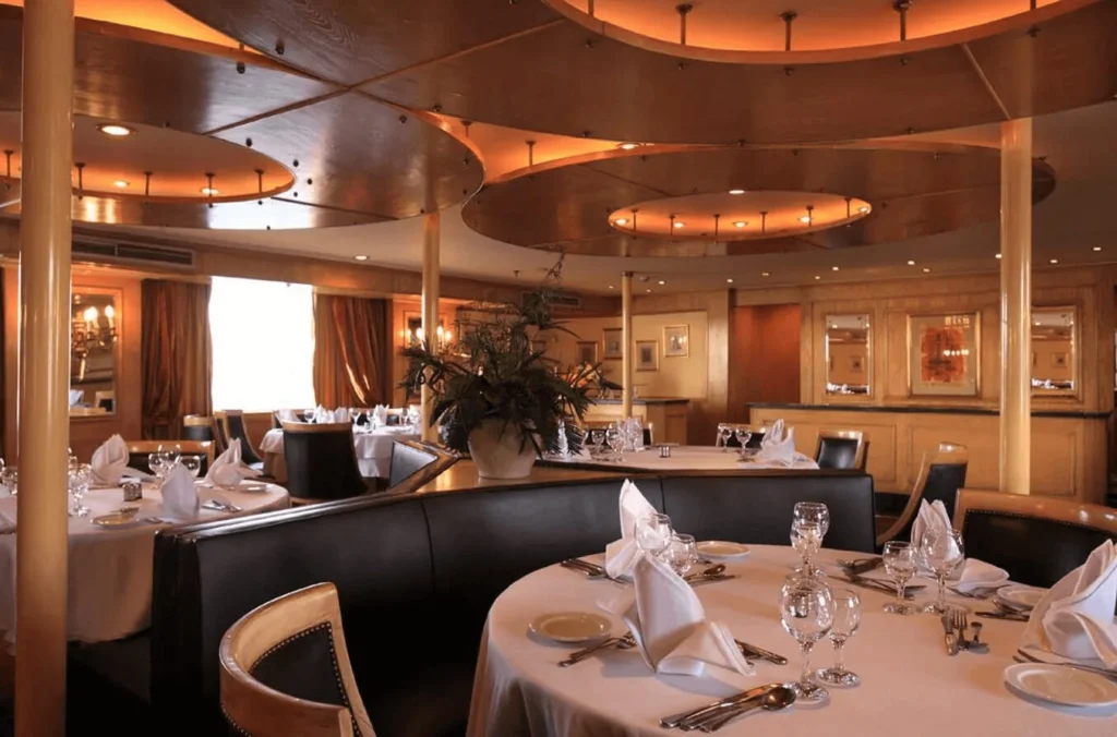 Tables laid with white linen and fan-folded napkins in the Iberotel Amara Nile cruise restaurant, dark leather banquettes behind