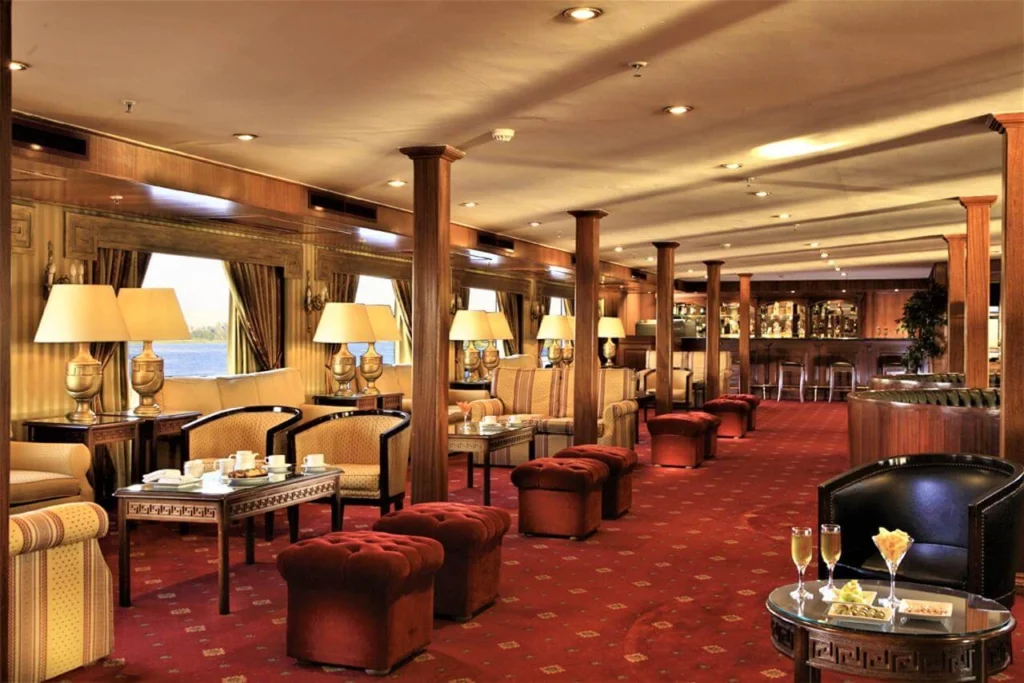 The bar lounge of the Iberotel Crown Emperor Nile cruise, table lamps and low chairs on a red carpet with the counter at the far end