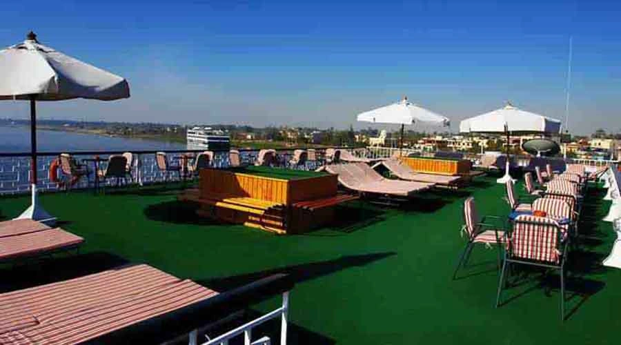 Loungers and parasols on the green matting of the Iberotel Helio Nile cruise sun deck, other cruisers moored across the water