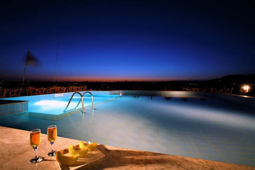 The lit swimming pool on the Jaz Crown Jewel Nile cruise sun deck at dusk, two glasses on the ledge in the foreground