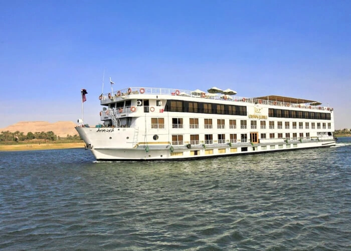 The Jaz Crown Jubilee Nile cruise ship on the Nile, a sandy escarpment rising on the far bank