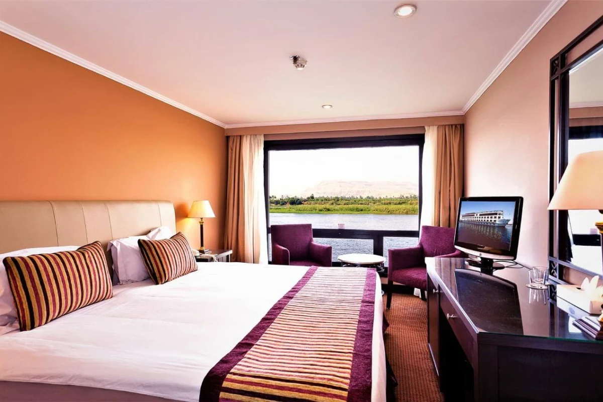 A double cabin on the Jaz Crown Prince Nile cruise with striped cushions, a desk and armchairs at a window onto the Nile