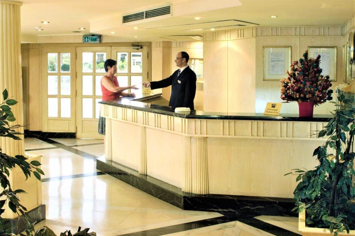 A guest being greeted at the reception desk of the Jaz Crown Prince Nile cruise, glass doors onto the deck behind