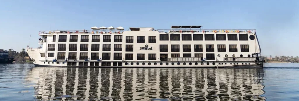 The Kleos Nile cruise ship at its mooring, its white hull and dark window bands reflected in the river