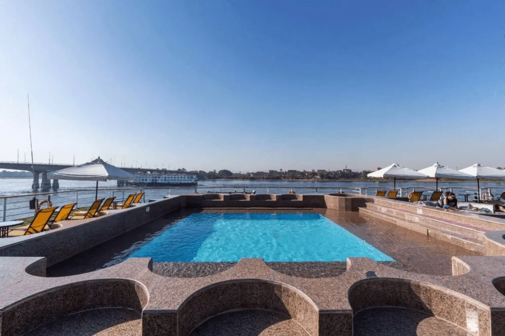 The swimming pool on the Kleos Nile cruise sun deck, yellow loungers along the granite surround and a bridge in the distance
