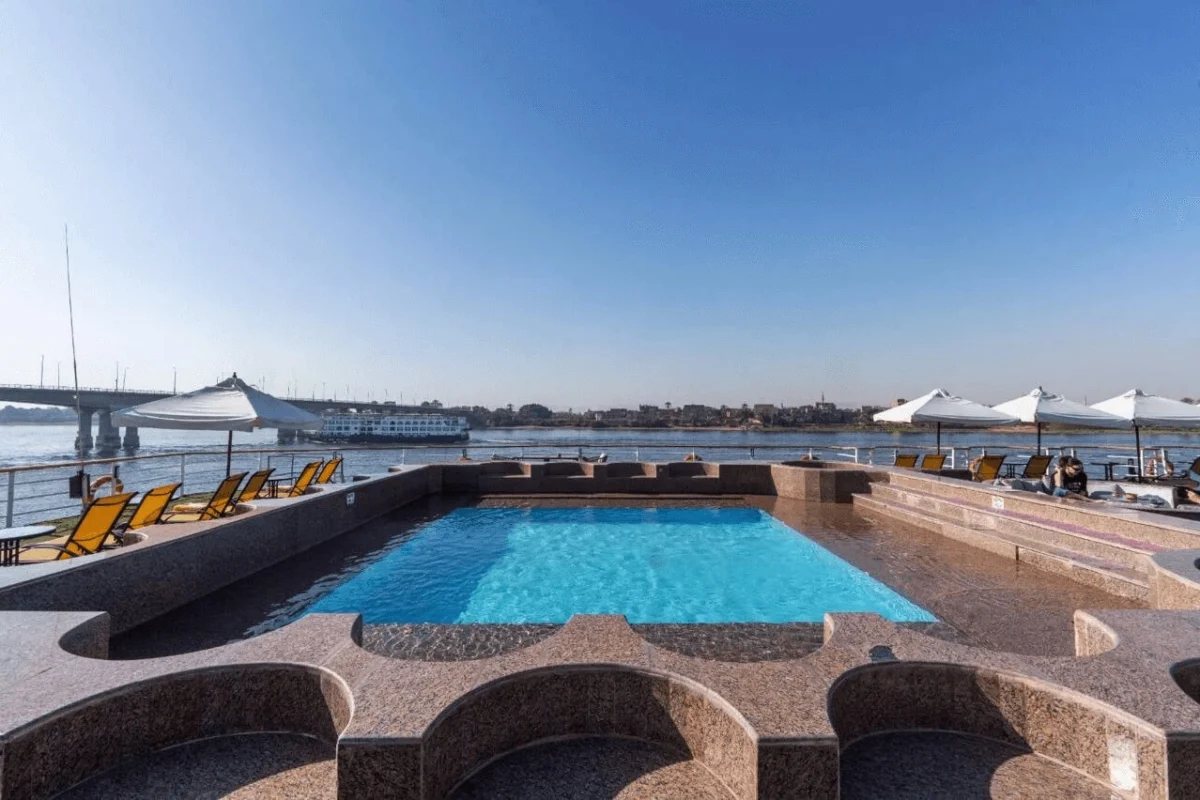 The swimming pool on the Kleos Nile cruise sun deck, yellow loungers along the granite surround and a bridge in the distance