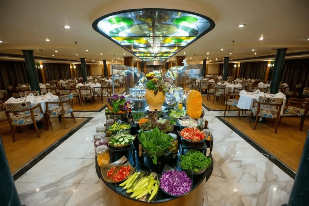 A salad and fruit buffet laid out on a round island in the Lady Mary Nile cruise restaurant, tables set beneath a stained-glass ceiling