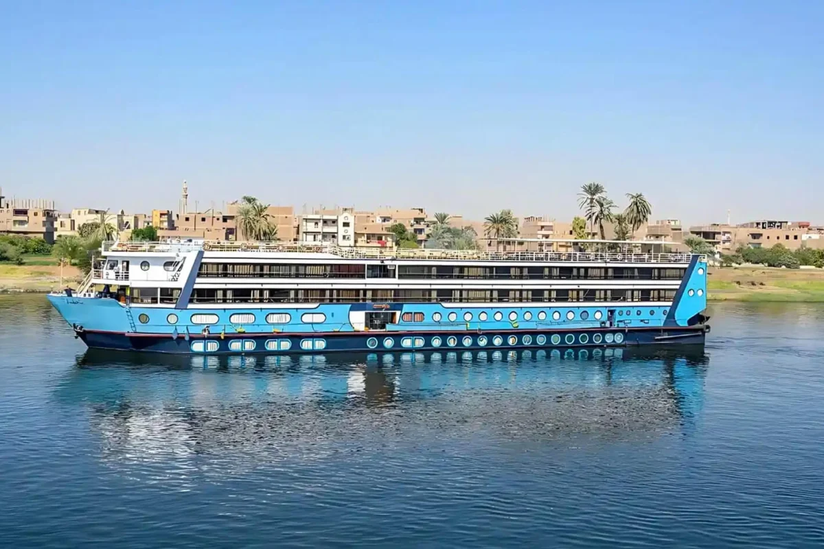 The Magic I Nile cruise ship on the Nile with its bright blue hull, a riverside town behind