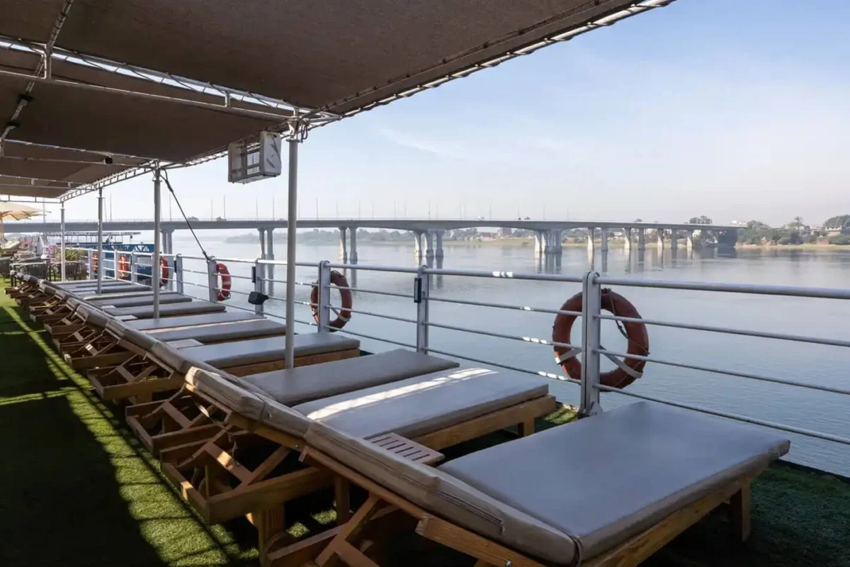 A row of loungers under the deck canopy of the Magic I Nile cruise, life rings on the rail and a bridge across the river beyond