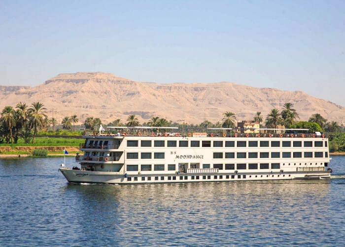 The Moon Dance Nile cruise ship on the Nile with palms on the near bank and the Theban hills rising behind