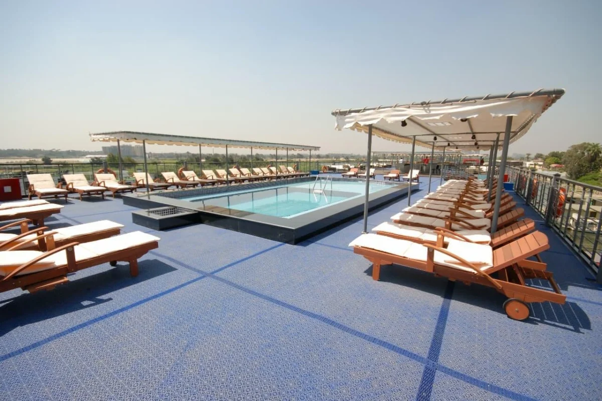 Timber loungers around the pool on the Moon Dance Nile cruise sun deck, green fields along the bank beyond