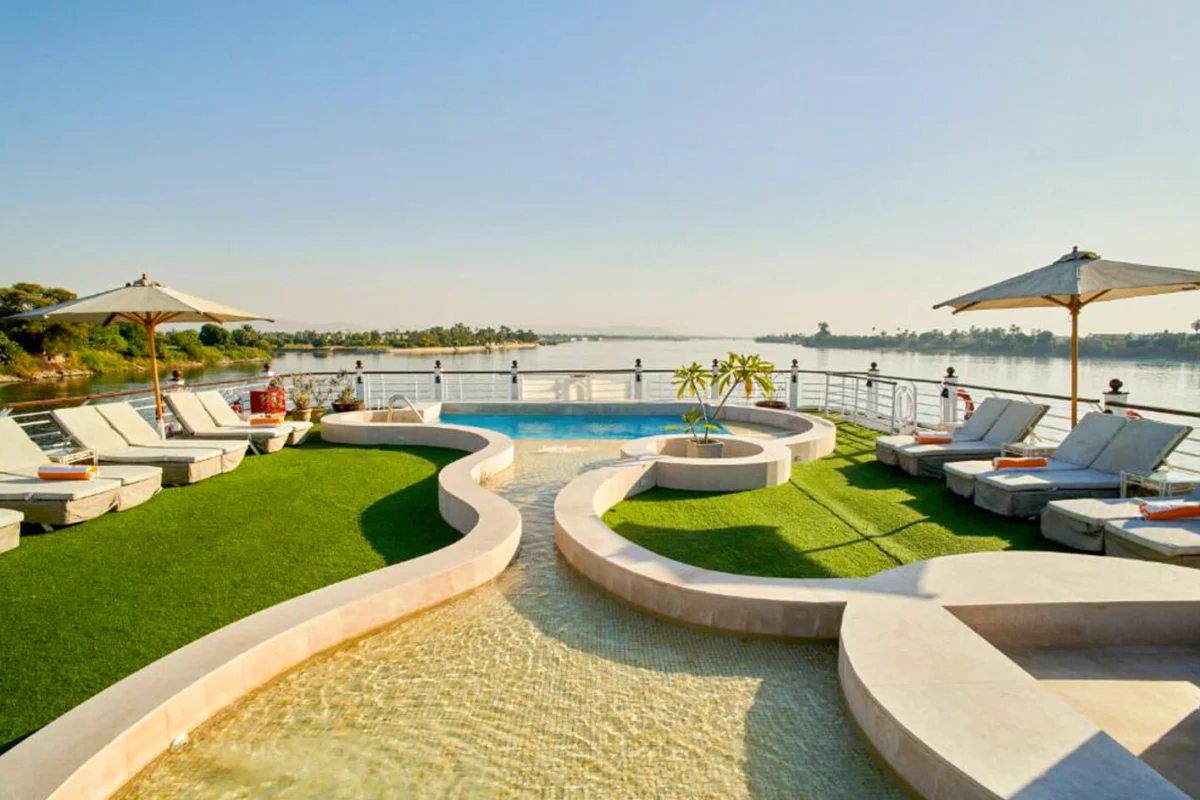 The curved swimming pool on the Movenpick Royal Lotus Nile cruise sun deck, loungers on green lawn and parasols along the rail