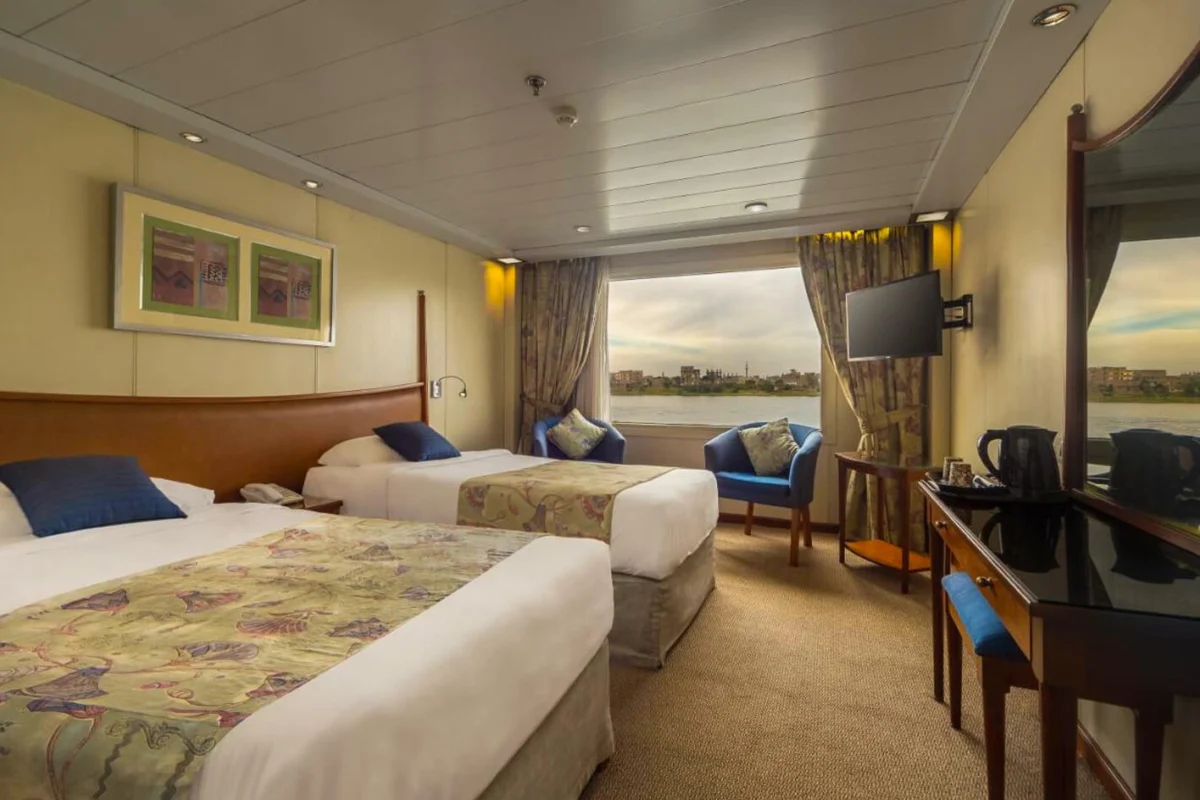 A twin-bed cabin on the Movenpick Royal Lotus Nile cruise with patterned covers, a desk and an armchair at the river window