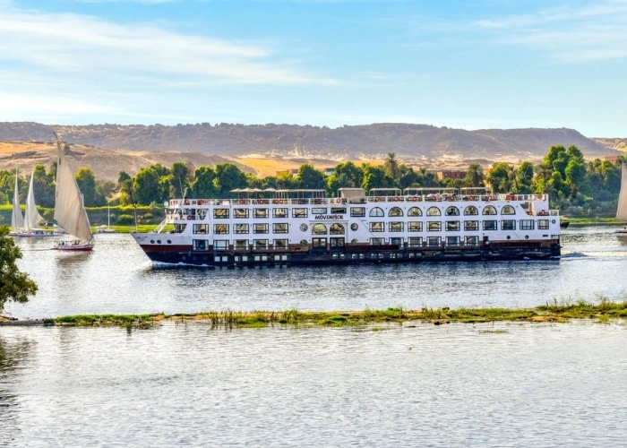 The Movenpick MS Sun Ray Nile cruise ship broadside on the Nile below desert hills, feluccas on the water around it