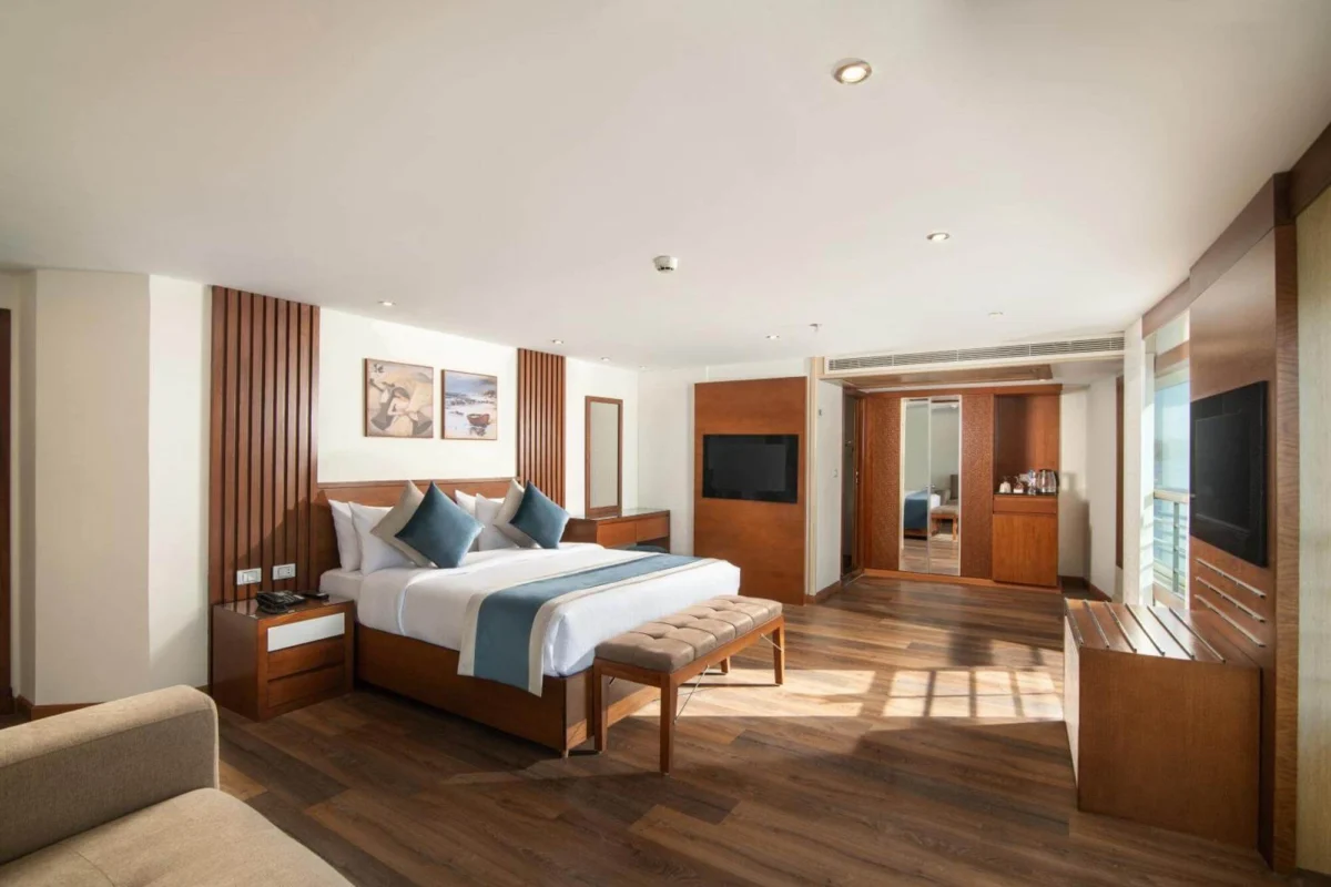 A suite on the Nile Capital Nile cruise with a wide bed, a bench at its foot and a wall-mounted television on timber panelling