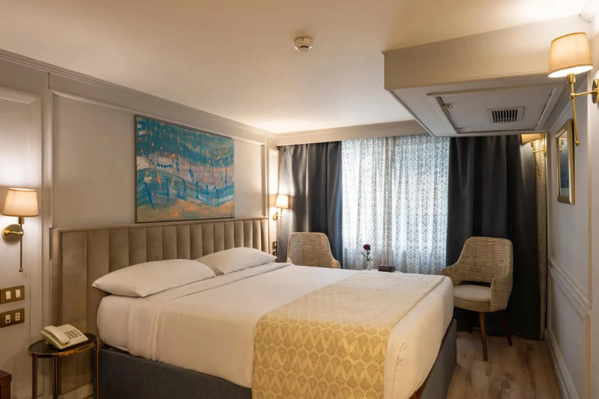 A double cabin on the Nile Excellence Nile cruise with a padded headboard, an armchair and a curtained river window