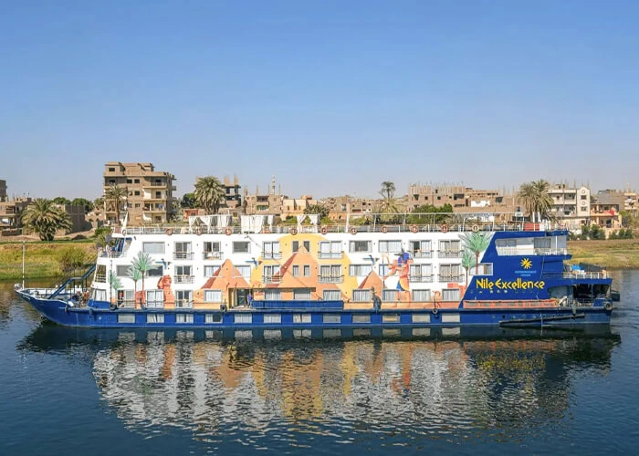 The Nile Excellence Nile cruise ship on the Nile, its blue hull and painted upper deck against a riverside town