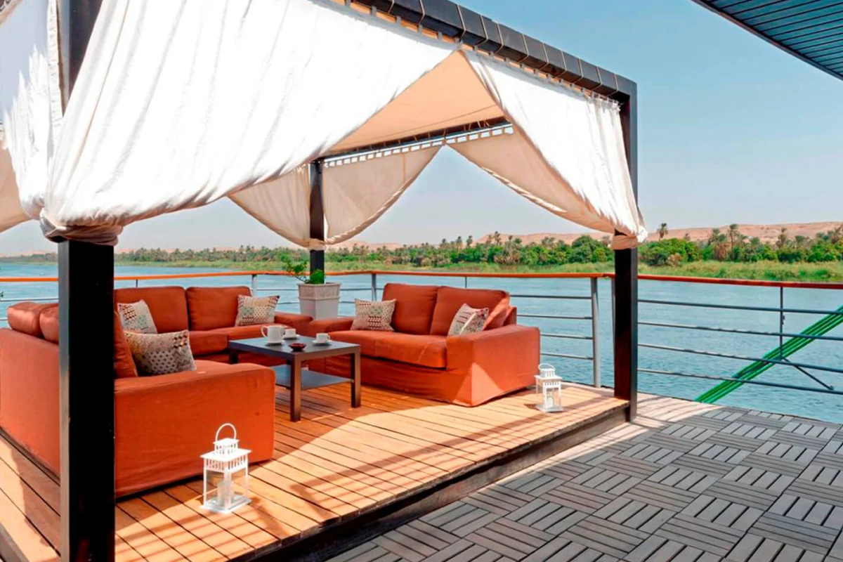An orange corner sofa under a curtained canopy on the Nile Premium Nile cruise deck, looking out across the river