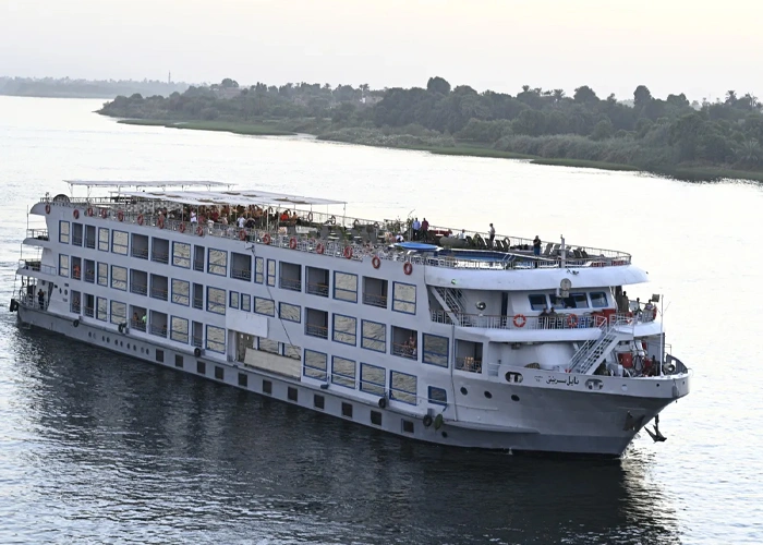 The Nile Serenity Nile cruise ship under way on the Nile, a wooded bank stretching behind it
