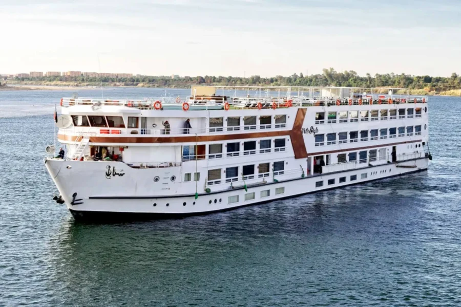 The Nile Style Nile cruise ship on the Nile seen from the bow quarter, a green bank behind it