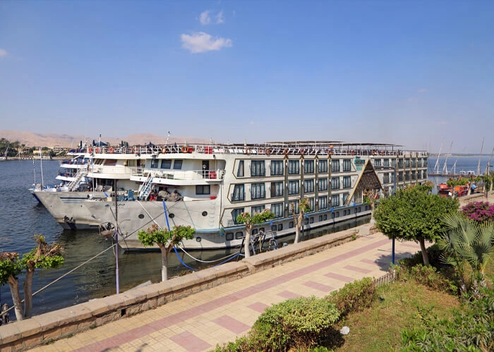 The Princess Sarah II Nile cruise ship moored at the quay beside other cruisers, a planted promenade in the foreground