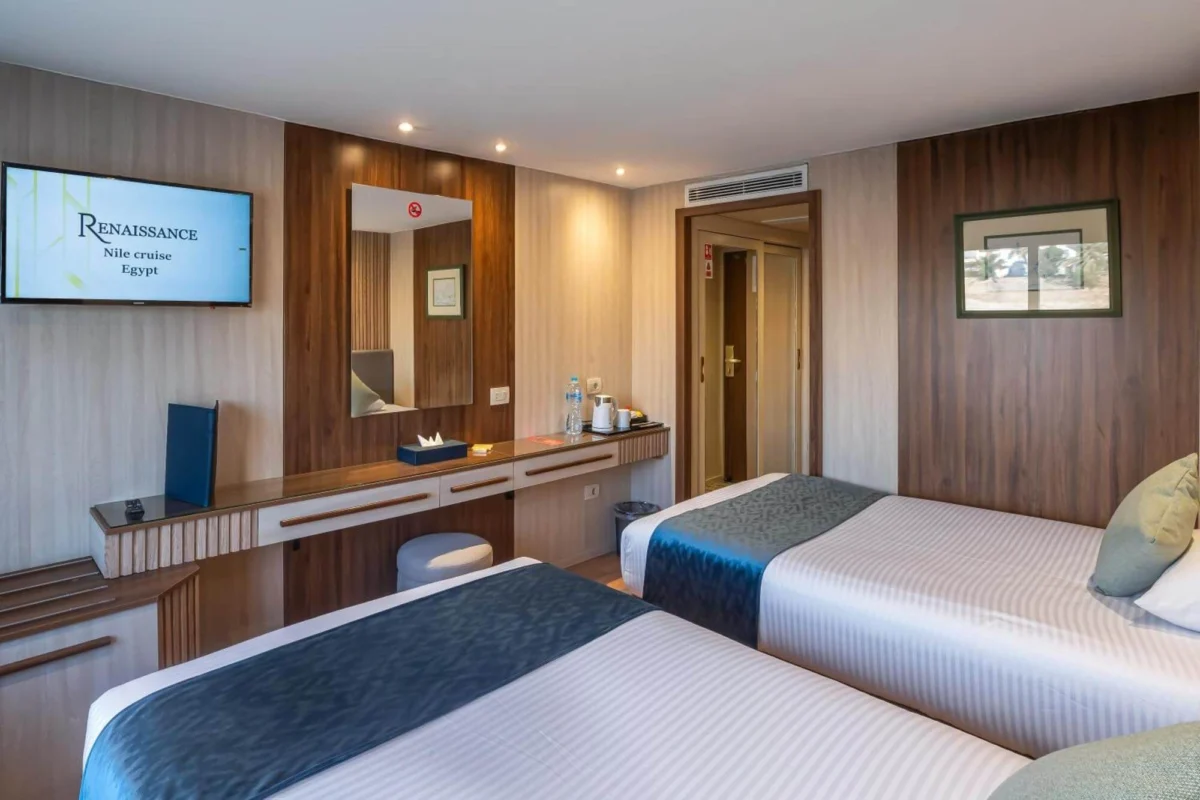 A twin-bed cabin on the Renaissance Nile cruise with navy runners, a long desk and a wall-mounted screen