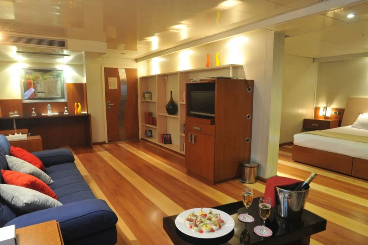 A suite on the Royal Esadora Nile cruise with a blue sofa, a timber media unit and a bed beyond