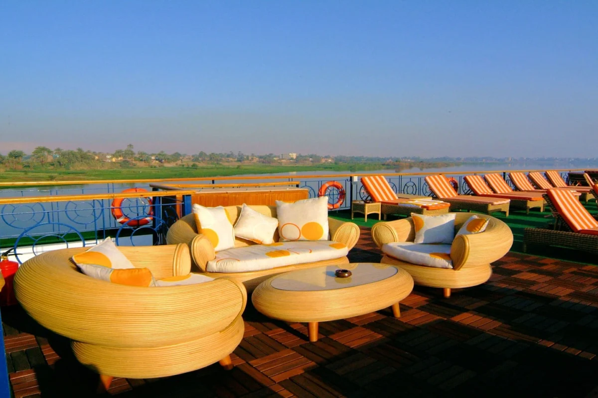 Curved cream daybeds on the Royal Esadora Nile cruise sun deck, loungers behind and green fields along the bank