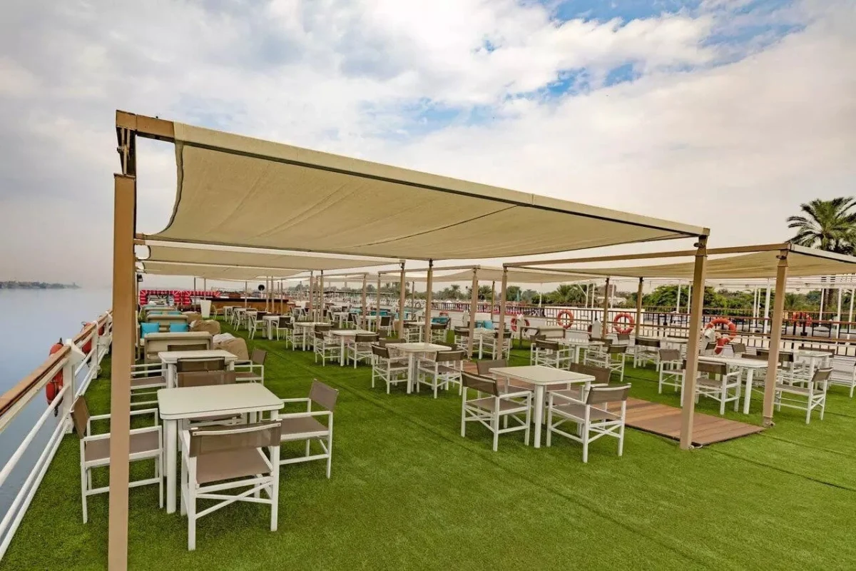White tables and chairs under a canvas shade on the Semramis II Nile cruise deck, green matting underfoot